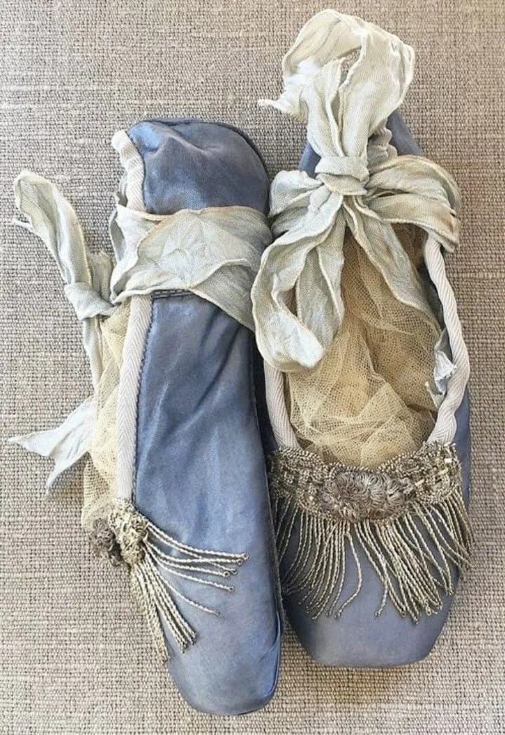 Pair of faded blue satin ballet slippers with silver fringe and ribbon ties on linen